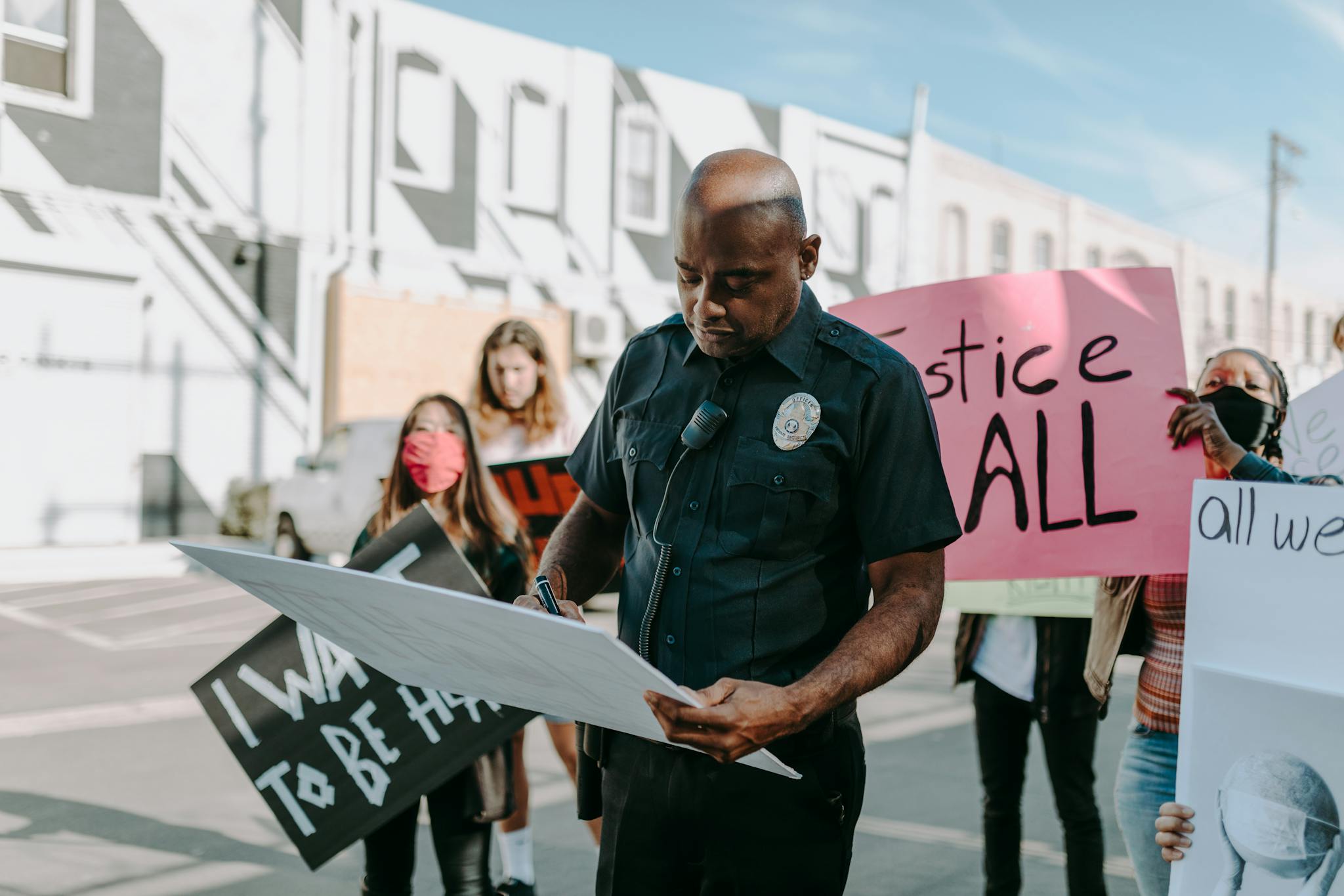 A diverse group of protesters engaging peacefully with a police officer holding a sign during a daytime demonstration.