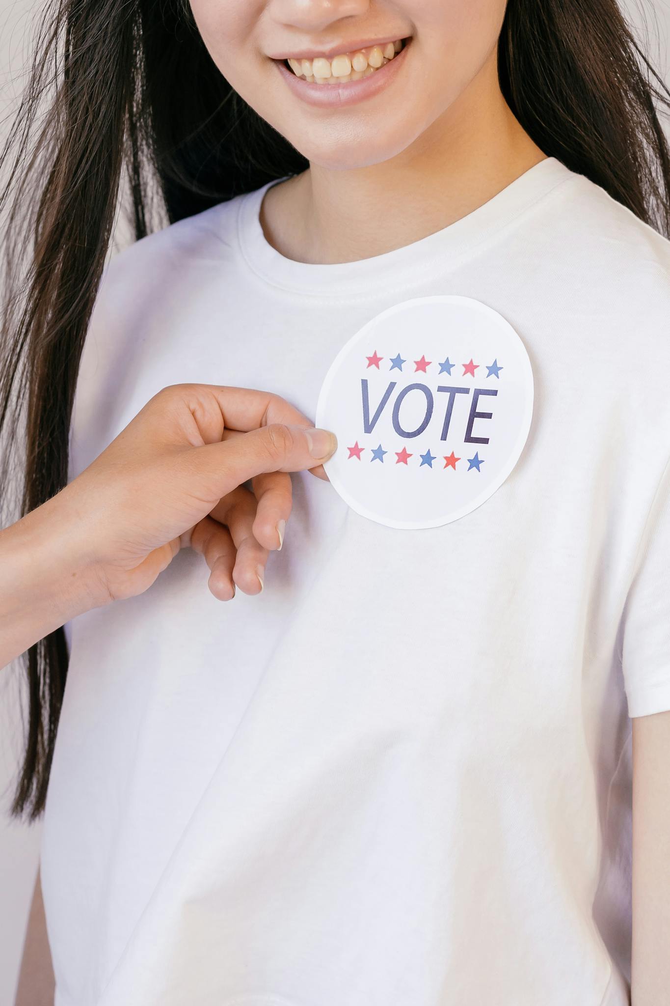 A person placing a round vote sticker on a white shirt, promoting political participation.